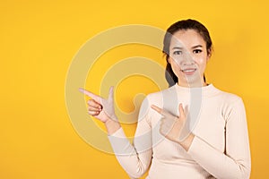 Portrait of smiling Asian woman wears cream sweater pointing finger to the side isolated on