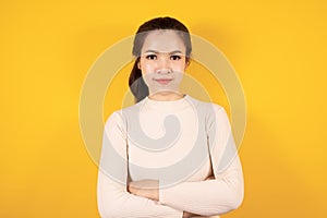 Portrait of smiling Asian woman wears cream sweater standing crossed arms isolated on yellow