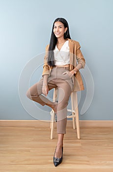 Portrait of smiling an attractive Asian businesswoman waring brown suit cool chic while sitting on chair and looking at camera