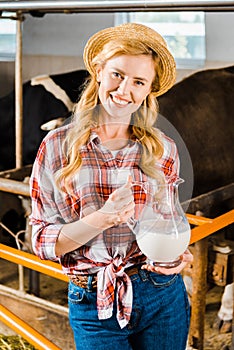 portrait of smiling attractive farmer holding jug of milk in stable and looking