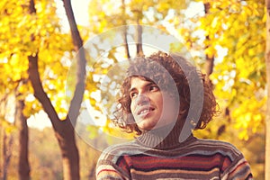 Portrait of smiling attractive man dressed in striped sweater, oudoor in autumn park.