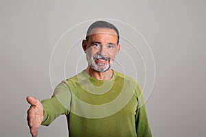 Portrait of smiling attractive old european man greets with hand, isolated on gray studio background