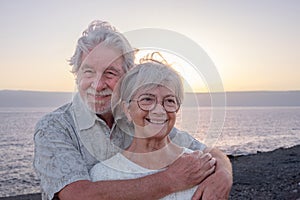 Portrait of smiling attractive senior couple embracing on the beach enjoying sea vacations - caucasian man and woman in love at