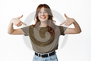 Portrait of smiling attractive woman pointing at herself, showing logo on center t-shirt, demonstrate advertisement with