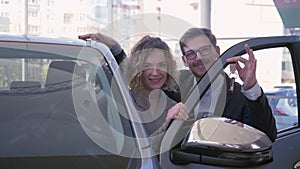 Portrait of smiling auto buyers, young couple enjoying automobile and showing keys car at sales center close-up