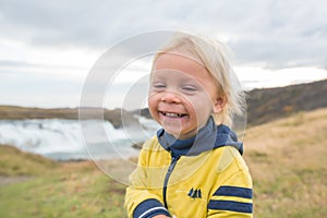 Portrait of a smiling baby boy near smaller waterfall around Gullfoss, Iceland