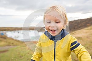 Portrait of a smiling baby boy near smaller waterfall around Gullfoss, Iceland