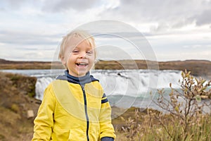 Portrait of a smiling baby boy near smaller waterfall around Gullfoss, Iceland