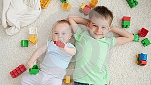 Portrait of smiling baby boy with older brother playing toy bricks and blocks while lying on carpet. Concept of children