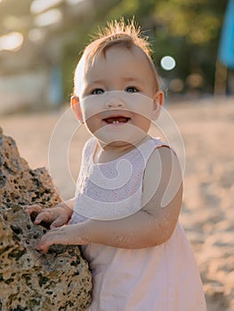 Portrait of smiling baby girl in pink dress on ocean beach with sunset sunshine