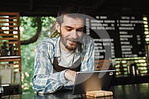 Portrait of smiling barista man using tablet computer while working in street cafe or coffeehouse outdoor