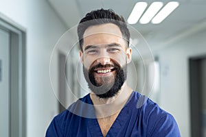 Portrait of smiling bearded caucasian male healthcare worker in hospital corridor, copy space