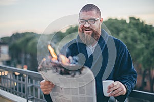 Portrait of smiling bearded man looking to the newspaper on fire - burning magazine in man`s hands
