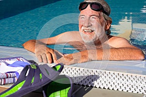 Portrait of a smiling bearded senior man doing sport in swimming pool. Sun on the face. Healthy lifestyle in retirement