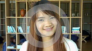 Portrait of smiling beautiful asian student standing in library. Bookcase bookshelves in background