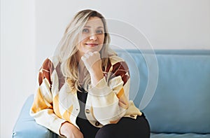 Portrait of smiling beautiful middle-aged woman with blonde hair sitting on sofa at home