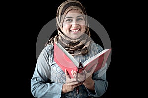 Portrait of smiling beautiful Muslim young woman wearing hijab scarf, reading Muslim book Quran holy Koran book of Islam in her