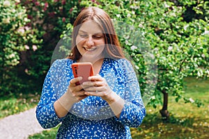 A portrait of a smiling beautiful person texting sms with her phone on nature background. Happy woman is using a