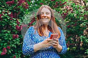 A portrait of a smiling beautiful person texting sms with her phone on nature background. Happy woman is using a