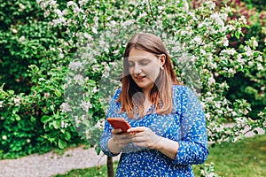 A portrait of a smiling beautiful person texting sms with her phone on nature background. Happy woman is using a