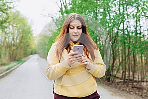 A portrait of a smiling beautiful redhead woman texting sms with her phone on nature background. Happy woman is using a