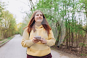 A portrait of a smiling beautiful redhead woman texting sms with her phone on nature background. Happy woman is using a