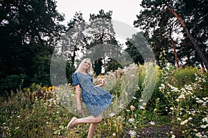A portrait of a smiling beautiful slender girl with blond long hair holding wildflowers