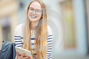 Portrait of a smiling beautiful teenage girl with dental braces. Young schoolgirl with school bag and tablet device