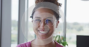 Portrait of smiling biracial creative businesswoman wearing glasses in modern office interior