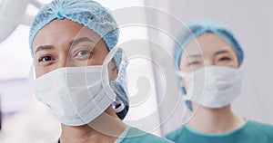 Portrait of smiling biracial female surgeon in cap and face mask in operating theatre, copy space