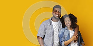 Portrait of smiling black couple hugging and posing over yellow background