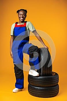 Portrait of smiling black female mechanic posing with new car tyres in studio