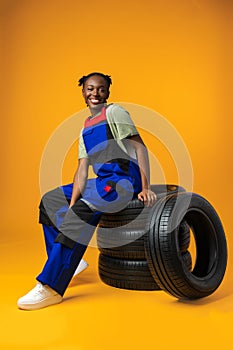 Portrait of smiling black female mechanic posing with new car tyres in studio