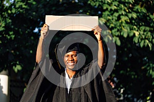 Portrait of smiling black guy standing with upraised empty cardboard poster on street looking for job, free copy space