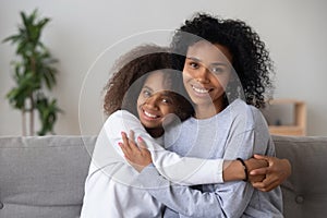 Portrait of smiling black mom and daughter hugging on couch