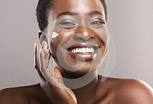 Portrait Of Smiling Black Woman Applying Moisturizing Cream on Face