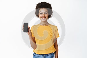 Portrait of smiling Black woman showing mobile phone screen, smartphone display and looking at camera, demonstrating