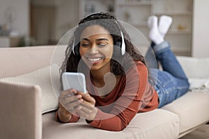 Portrait Of Smiling Black Woman Wearing Headphones Relaxing With Smartphone At Home