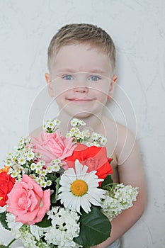 Portrait of smiling blond european cute boy with blue eyes on white background with a bouquet of flowers.