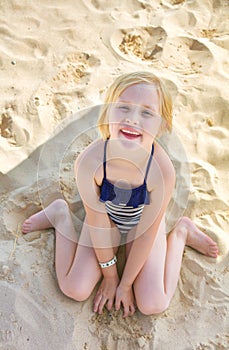 Portrait of smiling blond girl sitting in swimwear on beach