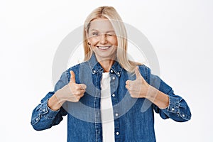 Portrait of smiling blond senior woman, grandmother shows thumbs up, approves smth, praise and compliment, stands over