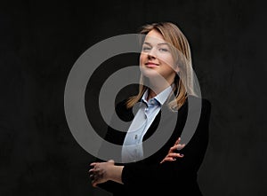 Portrait of a smiling blonde businesswoman formal dressed standing with crossed arms. Isolated on dark textured