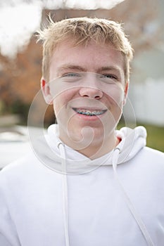 Portrait of smiling blonde teenage boy wearing a hoodie sweatshirt with braces on his face.