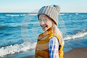Portrait of smiling blonde white Caucasian child kid girl with long hair, wearing yellow jacket gilet and grey hat