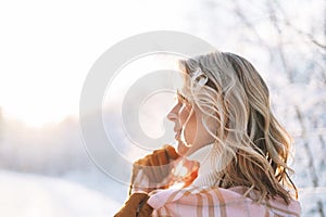 Portrait of smiling blonde woman in winter clothes in snowy winter forest in golden hour