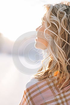 Portrait of smiling blonde woman in winter clothes in snowy winter forest in golden hour