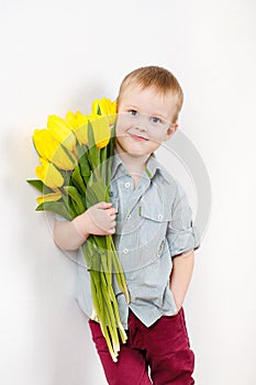 Portrait of Smiling boy with a bouquet of yellow tulips flowers in hands standing near white wall