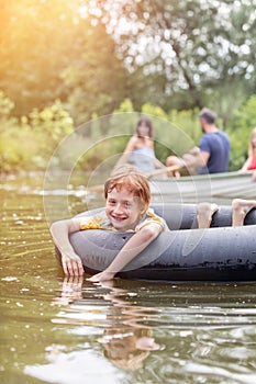 Portrait of smiling boy floating with inflatable ring against family boating in lake