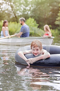 Portrait of smiling boy floating with inflatable ring in lake against family