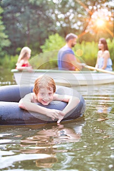 Portrait of smiling boy floating with inflatable ring in lake against family